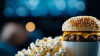 Fresh cheeseburger with sesame seed bun and melted cheese served with popcorn against blurred bokeh lights background, modern food photography.