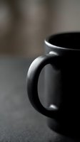 Black ceramic coffee mug with handle in artistic close-up shot with shallow depth of field and soft blurred background for kitchen and beverage concepts.