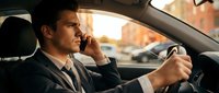 Professional businessman talking on phone while driving car during golden hour sunset commute in urban traffic setting.