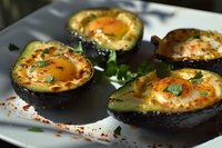 Baked avocado halves with eggs, herbs and spices on white plate. Healthy breakfast or brunch dish with protein and fresh ingredients for nutritious meal.