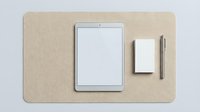 Minimalist workspace flatlay with tablet, blank screen, notepad, and pen on cork desk mat, top view, mockup for business or creative use.
