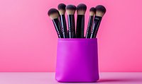 Professional makeup brushes set in purple leather holder against pink background, cosmetic tools arrangement for beauty artists and makeup application.
