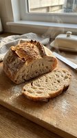 Freshly baked artisan sourdough bread loaf with rustic crust sliced on wooden cutting board in bright kitchen window light for homemade baking concepts.
