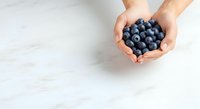 Female hands holding fresh blueberries on white marble surface, overhead view. Suitable for food, nutrition, health, wellness, and recipe content.