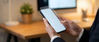 Professional businessman holding smartphone with blank white screen in modern office workspace for mobile app presentation and digital communication mockup.