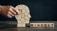 Senior businessman assembling wooden puzzle pieces forming human head with gears representing mindset development and cognitive problem-solving skills.