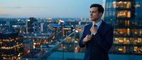 Professional businessman in dark suit standing on urban rooftop terrace overlooking illuminated city skyline at dusk for corporate leadership concepts.