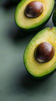 Fresh ripe avocado halves with large brown pits on dark background, macro shot showing detailed texture and natural gradient from yellow to green flesh.