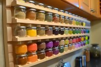 Colorful array of spices and seasonings in glass jars organized on wooden shelves, creating vibrant rows of culinary ingredients in home kitchen storage.