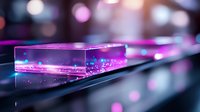 Glowing transparent acrylic block with pink and blue light effects against dark background, creating futuristic atmosphere with bokeh and reflective surfaces.