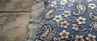 Vintage paisley pattern cushion with floral embroidery on rustic wooden background for home decor and interior design projects.