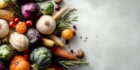 Fresh seasonal vegetables and herbs arranged on light background, colorful organic produce with artichokes, cabbage, pumpkin, carrots, and rosemary sprigs.