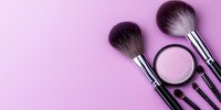 Professional makeup brushes and powder compact arranged on pink background with copy space, flat lay composition for beauty and cosmetics industry.