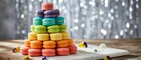 Colorful rainbow macarons stacked in pyramid on wooden table with bokeh lights background. French pastry dessert tower for bakery menu and celebration.