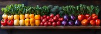 Fresh colorful vegetables and fruits arranged in rainbow order on rustic wooden table, including lettuce, persimmons, tomatoes, purple onions creating vibrant pattern.