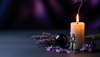 Mystical altar setup with burning candle, crystal ball, amethyst gems and lavender herbs on dark surface for spiritual rituals and fortune telling practices.