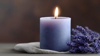 Glowing purple ombre candle with dried lavender sprigs on linen fabric creates peaceful spa atmosphere against dark background.