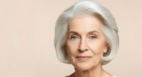 Senior woman with silver hair and fair complexion smiling at camera against neutral beige background for portrait and healthcare advertising.