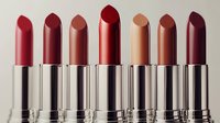 Row of luxury lipsticks in various shades from coral to deep burgundy arranged on neutral background for cosmetic and beauty product marketing.