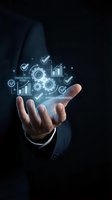 Businessman in dark suit holding glowing digital interface with gears, checkmarks, charts and productivity icons on black background. Business solutions concept.