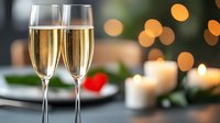 Two elegant champagne flutes filled with sparkling wine against blurred festive background with bokeh lights and burning candles, romantic celebration setting.