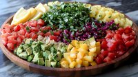 Colorful rainbow salad bowl with diced vegetables, herbs and cheese arranged in sections on wooden plate for healthy eating and meal prep.