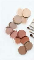 Makeup powder palette with neutral brown and beige eyeshadow shades scattered on white background with cosmetic brushes for beauty routine.