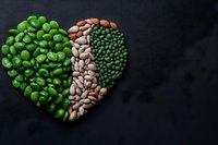Heart shape made from various legumes and beans on black background, including green peas, white and red kidney beans, arranged in decorative pattern.