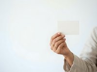 Close-up of a Caucasian male hand holding a blank cream-colored business card or note against a white background. Ideal for corporate branding, business communication, and marketing materials.