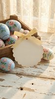 Painted Easter eggs in rustic wooden basket with blank gift tag and yellow ribbon on weathered white wood surface near lace curtain window for spring holiday.