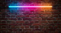 Vibrant neon light tube glowing with blue, purple, pink and orange colors against rustic brick wall background for modern interior design and lighting.