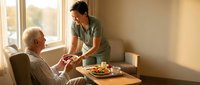 Young Asian female caregiver serving healthy meal to elderly Caucasian man in comfortable home setting with natural window light for healthcare services.