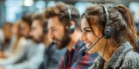 Diverse customer service team with headsets working in modern call center, smiling female agent providing professional support in foreground.