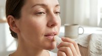 Middle-aged Caucasian woman applying lip balm in bright bathroom mirror, natural skincare routine, morning beauty ritual, self-care wellness lifestyle.