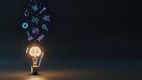 Glowing light bulb with floating science icons and symbols on dark background representing innovation, creativity and scientific discovery in education.