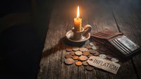 Burning candle with scattered coins and inflation paper tag on dark wooden table representing economic crisis and financial hardship concept.