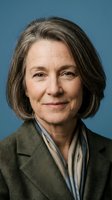 Mature woman with shoulder-length gray hair wearing olive blazer and scarf against blue background. Professional headshot suitable for corporate, business, and editorial use.