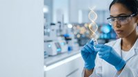 Young female scientist examining DNA double helix model in modern laboratory wearing safety glasses and gloves for genetic research and biotechnology studies.