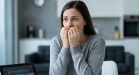 Anxious young Caucasian woman biting nails while working on laptop at home office desk, expressing stress and worry during remote work or online tasks.
