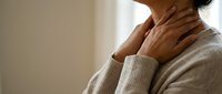 Woman touching neck experiencing throat pain or discomfort in cozy sweater at home for health and wellness concepts.