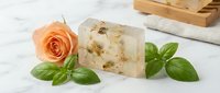 Handmade soap bar with oatmeal and botanical ingredients, displayed with fresh peach rose and basil leaves on marble surface for natural skincare and wellness product marketing.