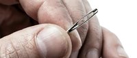 Closeup of male hands holding a sewing needle, showing detailed skin texture and fine motor control for tailoring, crafts, or healthcare applications.