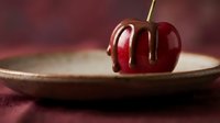 Fresh red cherry with chocolate drizzle on ceramic plate against burgundy background for gourmet dessert and culinary photography.