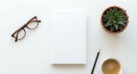 Minimalist workspace with blank paper, eyeglasses, succulent plant and coffee cup on white desk. Clean office setup for creative projects and planning.