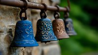 Decorative ceramic bells with ornate floral patterns in blue and brown tones hanging on rustic metal rod against blurred natural background. Traditional craft elements.