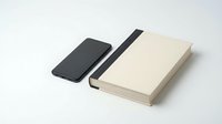 Smartphone with black screen and beige hardcover notebook with elastic band on white background, minimalist flat lay for business and productivity concepts.