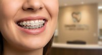 Close-up of young woman smiling with metal braces on teeth in modern dental office. Orthodontic treatment and oral healthcare concept.