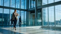 Professional businesswoman walking in modern glass office building lobby with smartphone, corporate architecture and urban cityscape view.