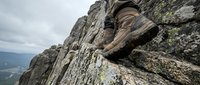 Hiker's boot on rocky mountain cliff edge with dramatic aerial valley view below, showcasing adventure, outdoor exploration, and rugged terrain climbing.