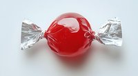 Red wrapped candy with silver foil ends on white background, isolated sweet treat close-up view for confectionery and food industry designs.